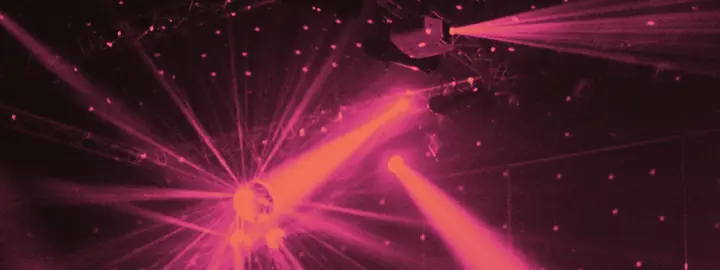 Una sfera a specchi e fasci di luce sopra una pista, in duotone magenta.